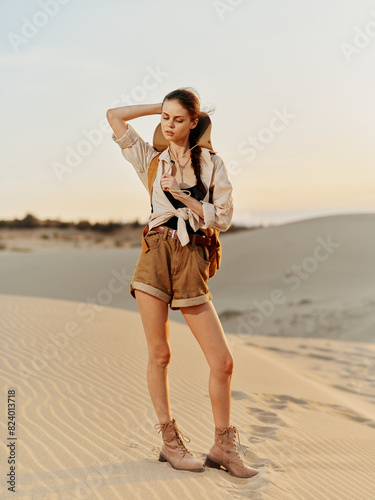 Woman in shorts and hat standing on sand dune in the desert under the clear blue sky