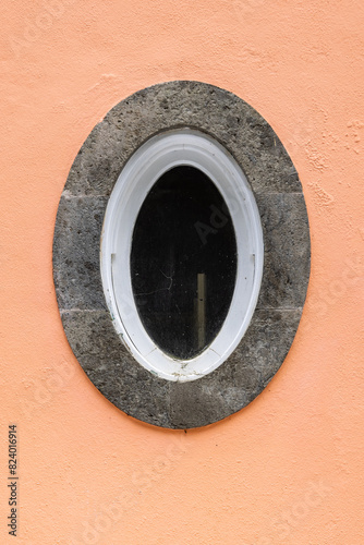 Oval window on a peach colored stuccoed building.