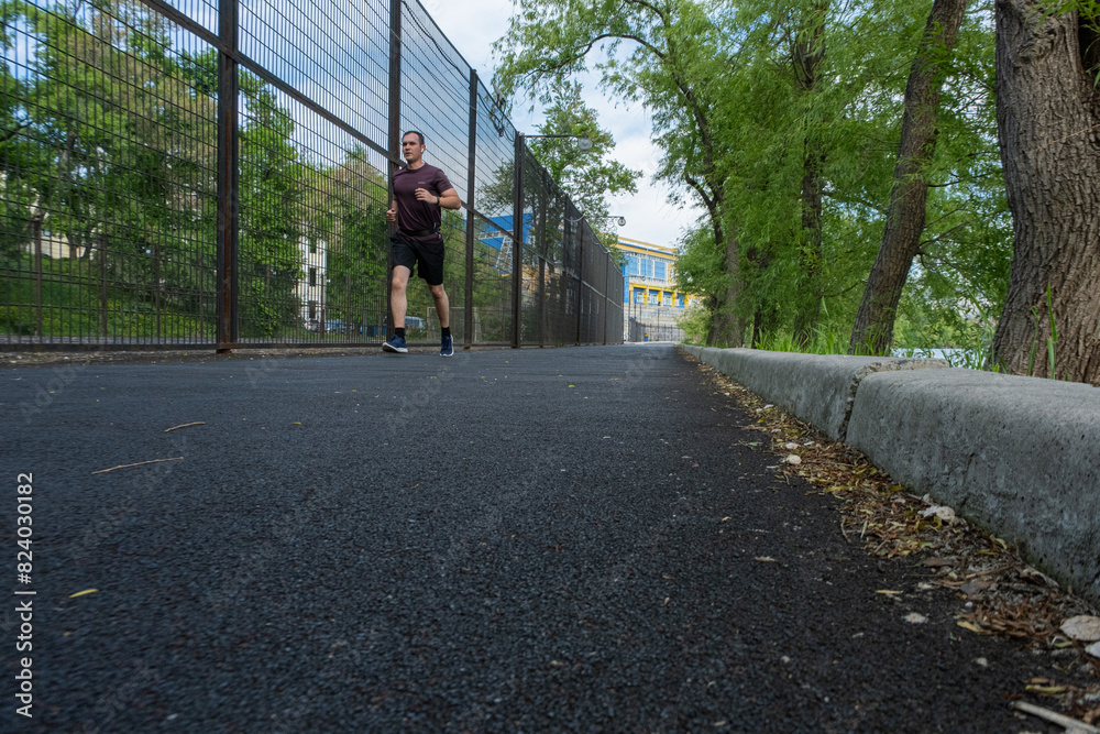 A young guy in an athletic uniform, wearing shorts runs straight down the rubber track. Sports on the street A young guy in an athletic uniform, wearing shorts runs straight down the rubber track. Sports on the street