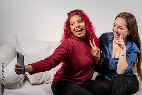 Par de amigas divirtiéndose y tomándose una selfie mientras están sentadas en un sofá photo