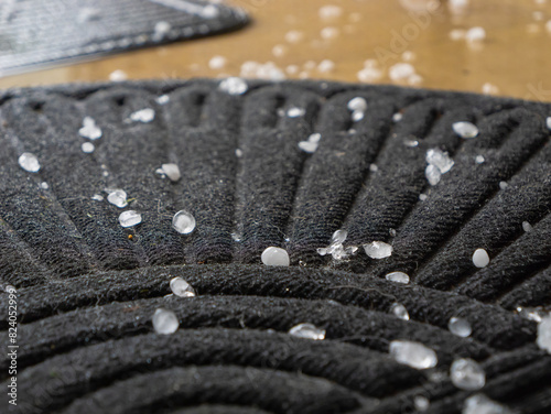CLOSE UP, DOF: Black doormat covered with hailstones after a heavy summer storm. A strong wind blew the precipitation all over the outdoor terrace. Intense stormy weather situations in summertime. photo