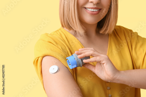 Woman with glucose sensor for measuring blood sugar level and applicator on yellow background. Diabetes concept