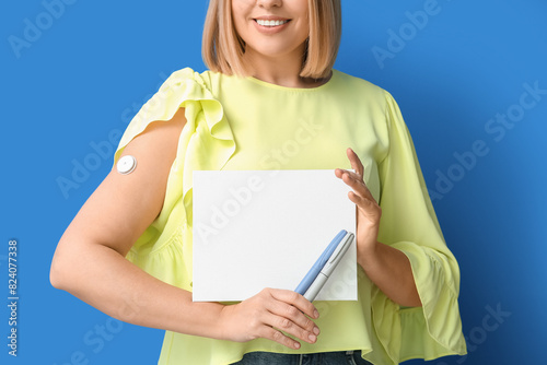 Woman with glucose sensor for measuring blood sugar level, lancet pens and blank paper on blue background. Diabetes concept