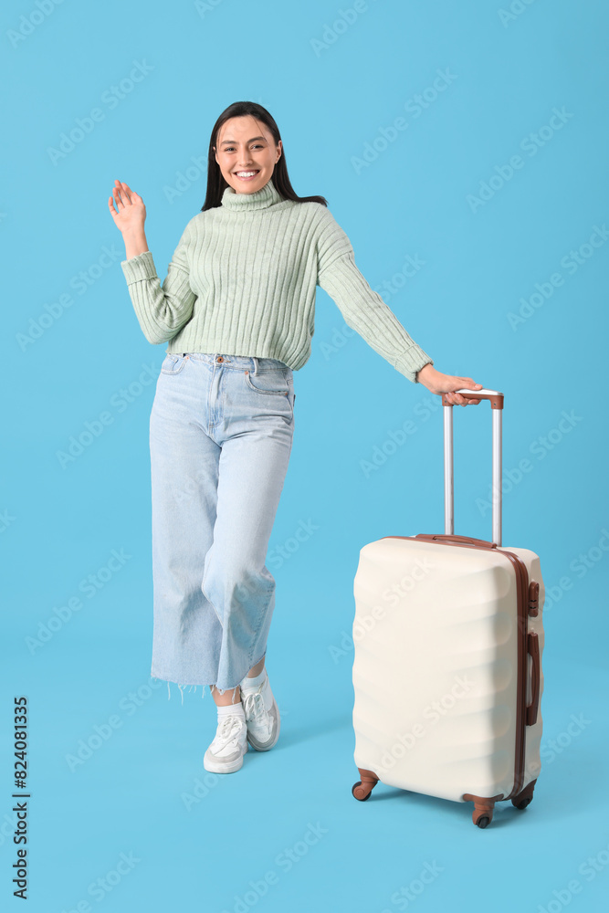Female tourist with suitcase waving hand on blue background Female tourist with suitcase waving hand on blue background