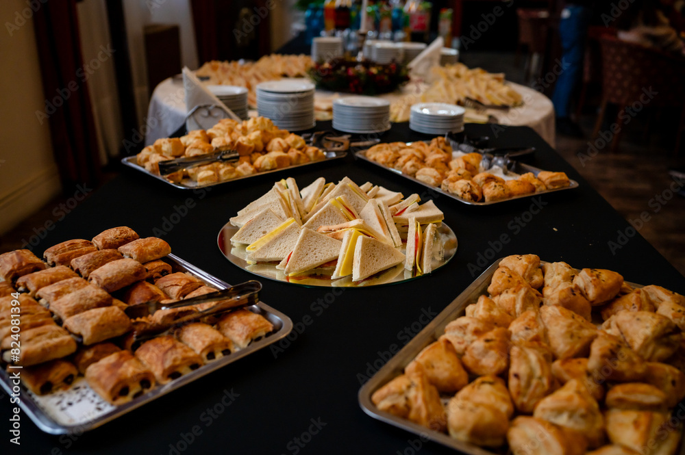 A table adorned with an array of food items. On the left, there are trays filled with golden-brown pastries, possibly croissants or pies. In the center, a plate holds neatly arranged triangular