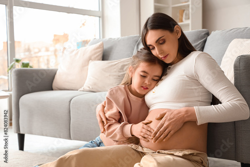 Young pregnant woman with her little daughter hugging at home photo