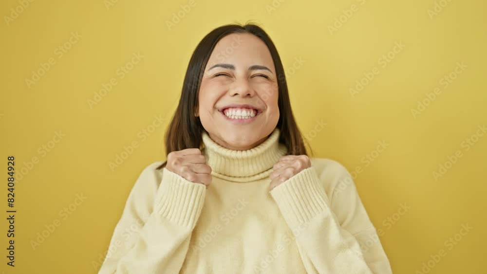 Joyful young hispanic woman, in sweater, celebrates sweet win with eyes closed, arms raised and smiling face on yellow isolated backdrop Joyful young hispanic woman, in sweater, celebrates sweet win with eyes closed, arms raised and smiling face on yellow isolated backdrop