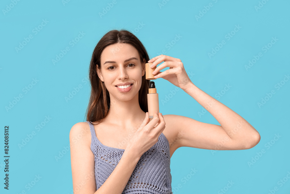Naklejka premium Beautiful young woman opening face foundation on blue background