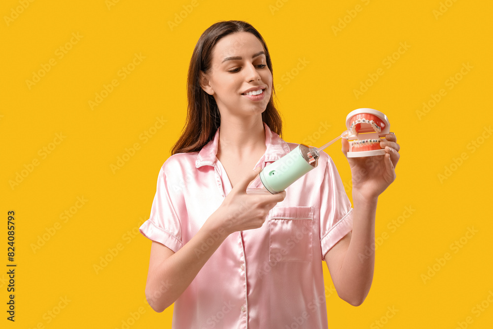 Beautiful young woman with oral irrigator and jaw model on yellow background Beautiful young woman with oral irrigator and jaw model on yellow background