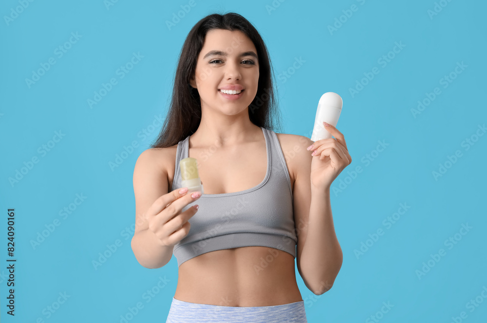 Happy smiling young woman with different deodorants on blue background Happy smiling young woman with different deodorants on blue background