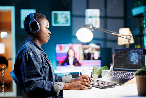 African American woman working on laptop, using AI to develop futuristic software system. Black female individual with her personal computer, showing her skill in programming and cyber security. photo