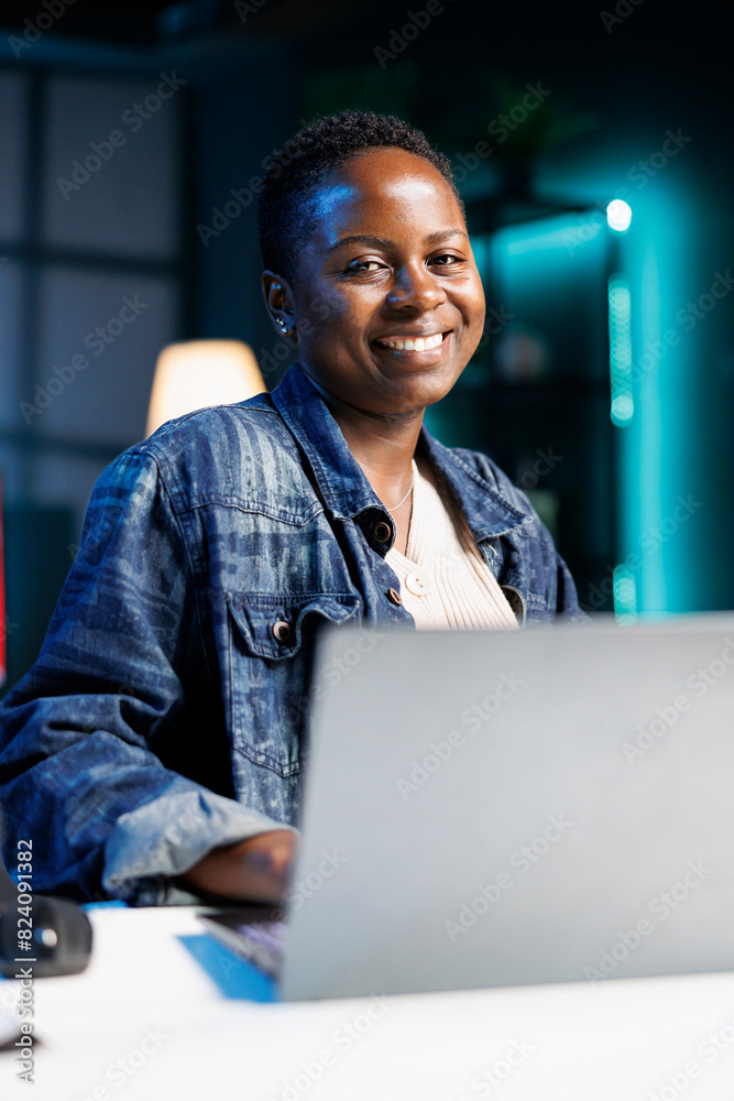 Portrait of African American blogger works on a laptop in a modern apartment. Smiling black woman is a dedicated freelancer, typing and reviewing information for her project. Portrait of African American blogger works on a laptop in a modern apartment. Smiling black woman is a dedicated freelancer, typing and reviewing information for her project.