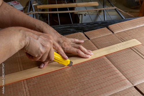Close-up of woman's hands cutting strips of corrugated cardboard along markings with stationery knife. Concept of recycling packaging into useful household item, DIY.