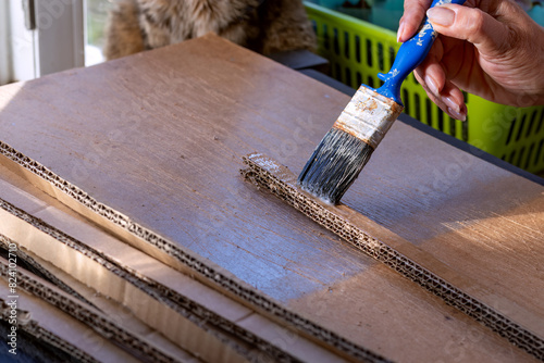 Corrugated cardboard stripes are glued together in several layers using PVA glue and brush. Recycling packaging into useful household item. Process of making temporary furniture from cardboard boxes