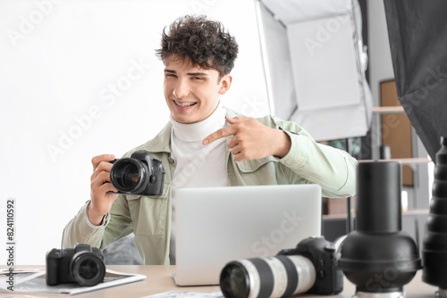 Professional happy male photographer with laptop pointing at modern cameras in studio