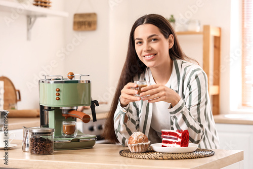 Beautiful young happy woman with modern coffee machine and desserts in kitchen