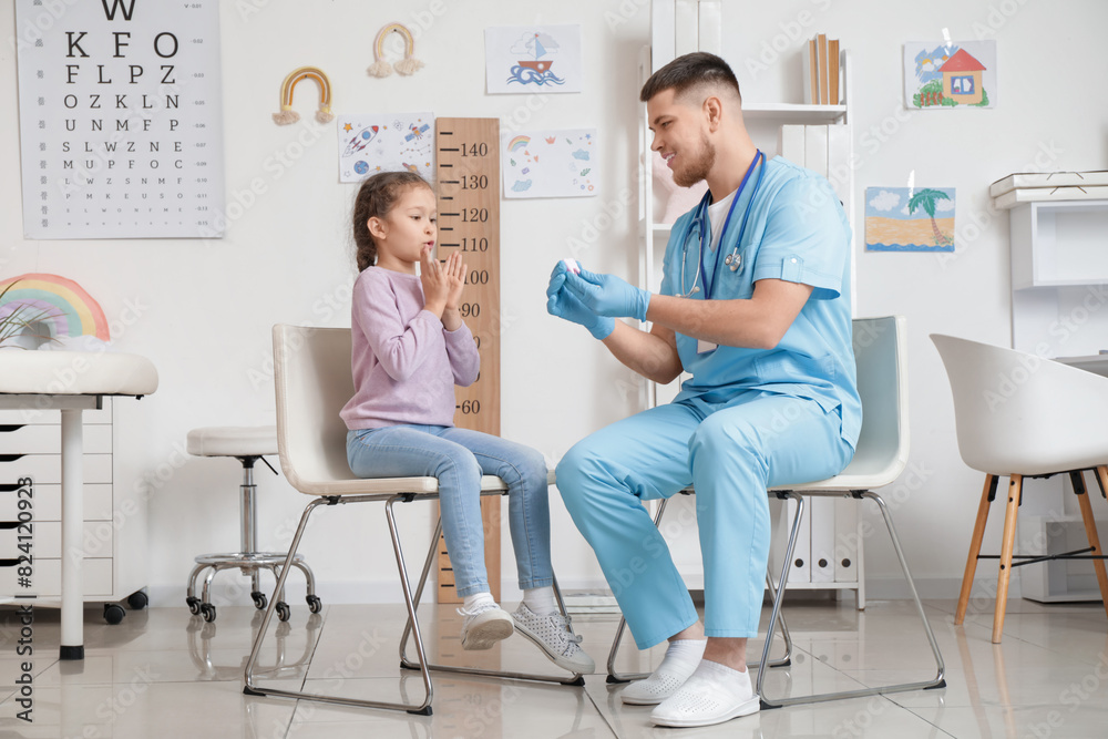 Obraz premium Male pediatrician showing plastic tooth to shocked little girl in clinic