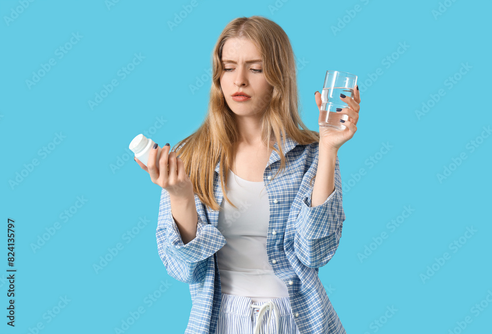 Tired young woman in pajamas with sleeping pills and glass of water on blue background Tired young woman in pajamas with sleeping pills and glass of water on blue background