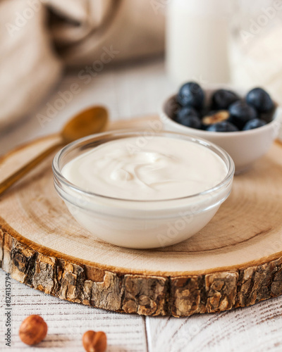 Rich creamy yogurt in a glass bowl on a wooden round, accompanied by fresh blueberries 