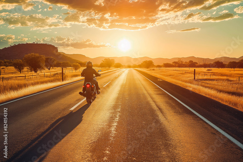 An Indigenous Australian motorcyclist cruises down a deserted highway on a powerful motorbike, with the last rays of the sun stretching long shadows on the road. © VisualProduction