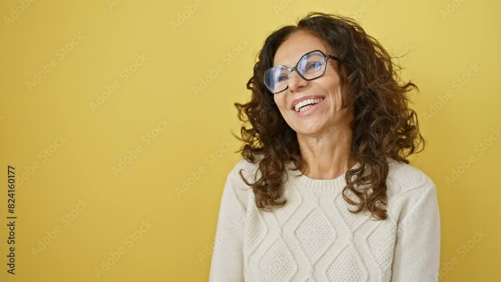 Cheerful middle-aged hispanic woman with a radiant smile, stylish glasses, confidently laughing away, standing against a vivid yellow isolated background. Cheerful middle-aged hispanic woman with a radiant smile, stylish glasses, confidently laughing away, standing against a vivid yellow isolated background.
