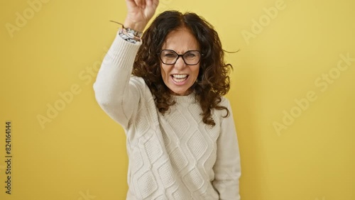 Furious, displeased middle age hispanic woman in glasses, angrily pointing at you on camera! a negative outburst against a yellow, isolated background. photo