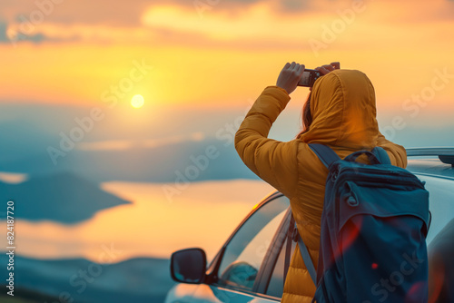 woman looking at the sea and mountains from the opened roof of her car. Taking photos of a beautiful sunset.