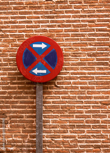 Red and blue traffic sign next to a brick wall.