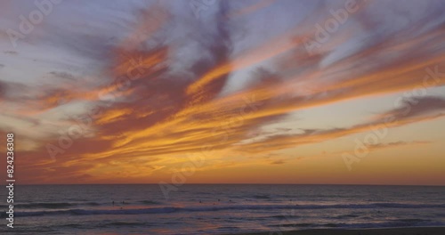 Tropical beach at sunset with dramatic orange sky and people swimming in ocean with calm waves photo