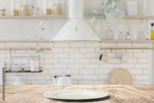 Empty white plate on rustic wooden table in a modern kitchen.