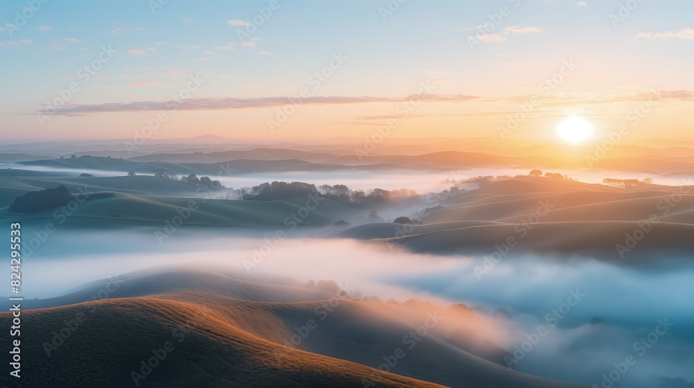A panoramic view of rolling hills covered in mist during a calm morning sunrise. 