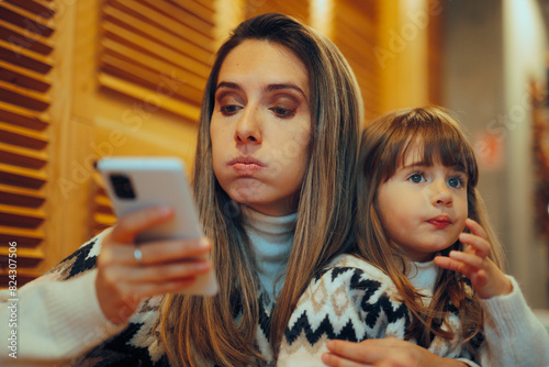 Mom Checking her Smartphone While Holding her daughter in Restaurant. Distracted mom being chronically online and absent minded 
 photo