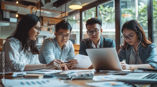 A group of young professionals are working together on a project. They are looking at a laptop and discussing something. They are all smiling and seem to be enjoying their work. The image is taken in