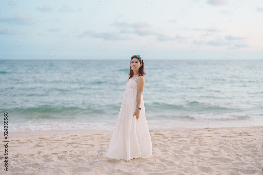 Happy traveler woman in white dress enjoy beautiful sea view, young woman standing on sand and looking ocean at tropical beach. Freedom, relaxing, vacation holiday and summer travel concept