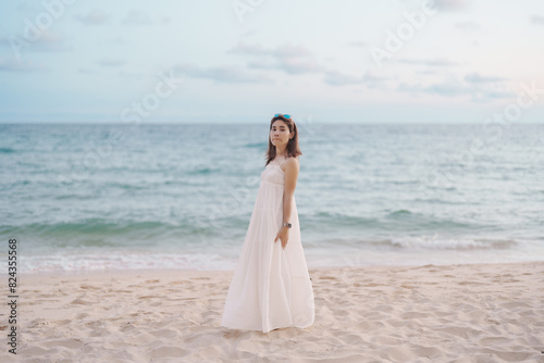 Happy traveler woman in white dress enjoy beautiful sea view, young woman standing on sand and looking ocean at tropical beach. Freedom, relaxing, vacation holiday and summer travel concept