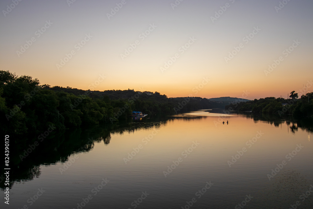 As the day gracefully transitions to dusk, Lady Bird Lake in Austin, Texas, becomes a canvas for nature's beauty. The serene river mirrors the warm tones of the setting sun.