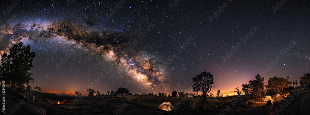 A stunning panoramic view of a camping site under a starry sky with the Milky Way spreading across the horizon.