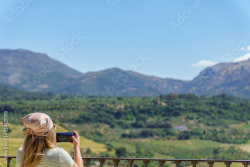 woman seen from the back with a headscarf taking pictures of a landscape with her mobile phone