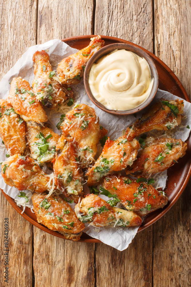 Chicken Parmesan Wings are oven-baked or air-fried and then coated in a buttery garlic parmesan sauce closeup on the plate on the table. Vertical top view from above