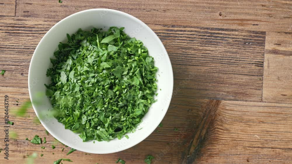 A chef sprinkles chopped fresh green parsley in a white bowl on wooden kitchen table to prepare a healthy meal, top view. Food close up A chef sprinkles chopped fresh green parsley in a white bowl on wooden kitchen table to prepare a healthy meal, top view. Food close up