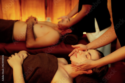 Couple customer enjoying relaxing anti-stress head massage and pampering facial beauty skin recreation leisure in warm candle lighting ambient salon spa in luxury resort or hotel. Quiescent