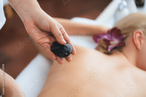 Hot stone massage at spa salon in luxury resort with day light serenity ambient  blissful woman customer enjoying spa basalt stone massage glide over body with soothing warmth. Quiescent
