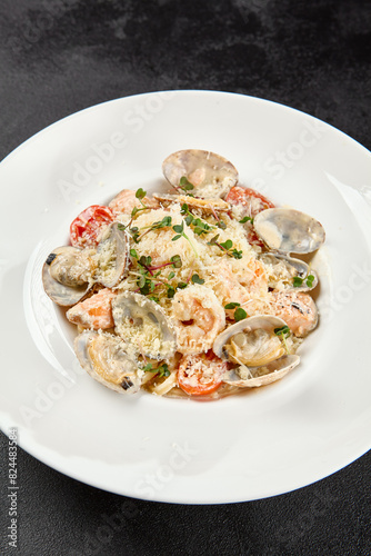 Seafood pasta with vongole, clams, salmon fish and prawns in white plate. Spaghetti marinara with seafood and cheese on dark background. Seafood menu - pasta in mediterrian style on black table.