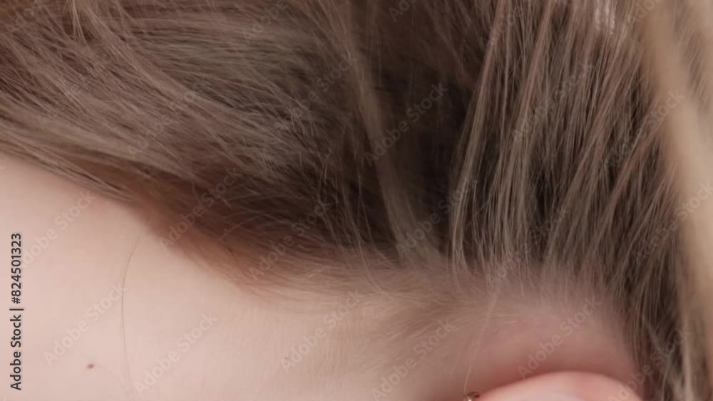Vertical video. A red-haired girl stands with her back in the studio on a gray background and waves her hair. The concept of caring for beautiful and healthy hair.