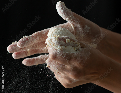 hands knead dough on a black background.