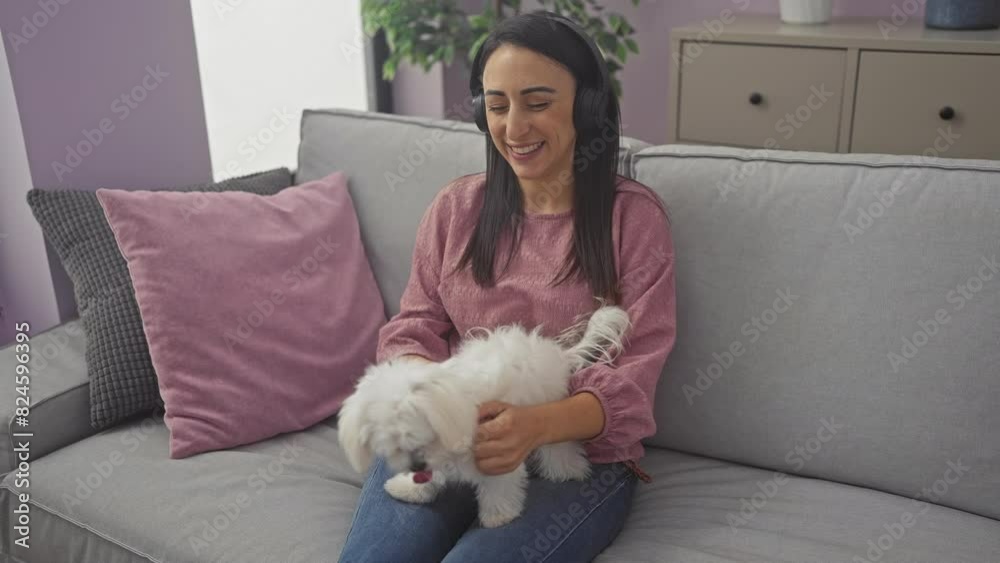 A smiling woman in headphones enjoys time with her bichon maltese dog on a cozy living room sofa. A smiling woman in headphones enjoys time with her bichon maltese dog on a cozy living room sofa.