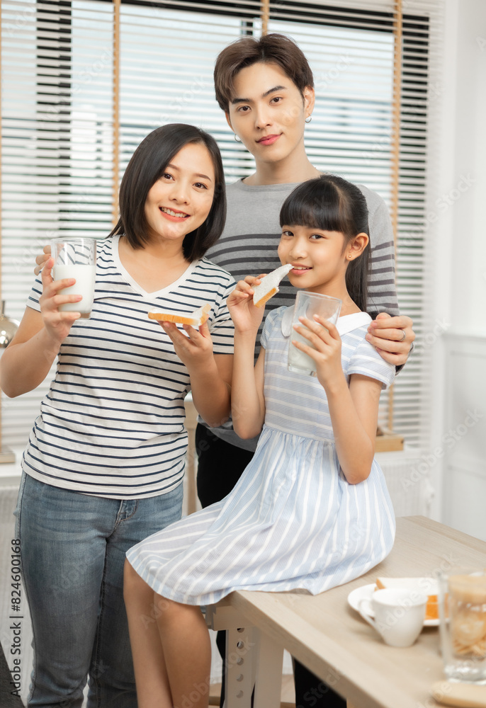 Parents and daughter enjoying breakfast with milk in a warm, inviting kitchen.Asian family breakfast scene, parents and daughter eating and drinking milk at home Parents and daughter enjoying breakfast with milk in a warm, inviting kitchen.Asian family breakfast scene, parents and daughter eating and drinking milk at home