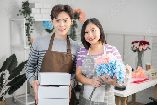 A couple of Asian entrepreneurs using their smartphones to sell flowers online.