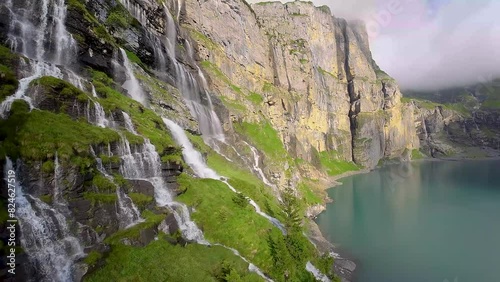Aerial flight next to a beautiful big waterfall on a mountain Landscape, Drone Flying Over a Blue Lake - Oeschinen Lake, Switzerland (ID: 824627519)