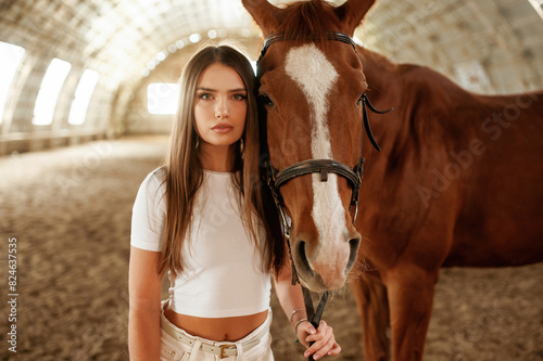 In white clothes, standing. Beautiful young woman is with horse indoors © standret